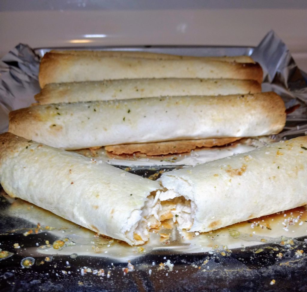 baked chicken taquitos broken in half with a creamy middle
